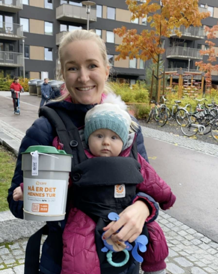 En mor står med bøsse og en baby i bæresele.
