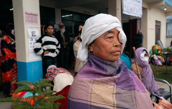 Kvinne i Nepal sitter med lapp foran øyet ved øyeklinikk. 