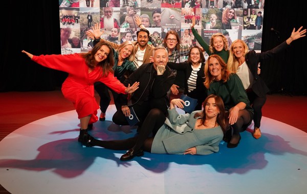 Programledere og deltakere fra TV-sendingen 2023 poserer sammen. Bak dem er en vegg med bilde av bøssebærere