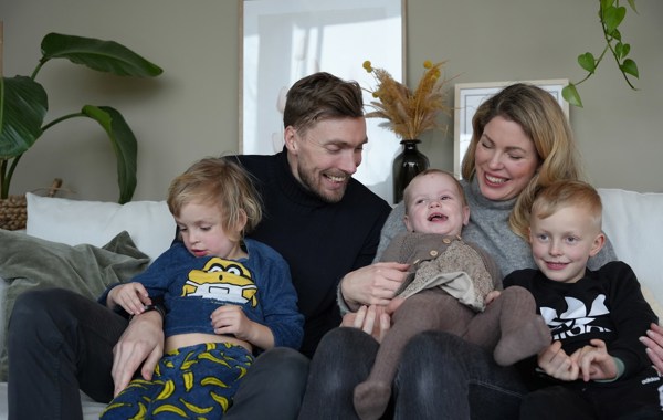 En familie på fem smiler og ler i en sofa.