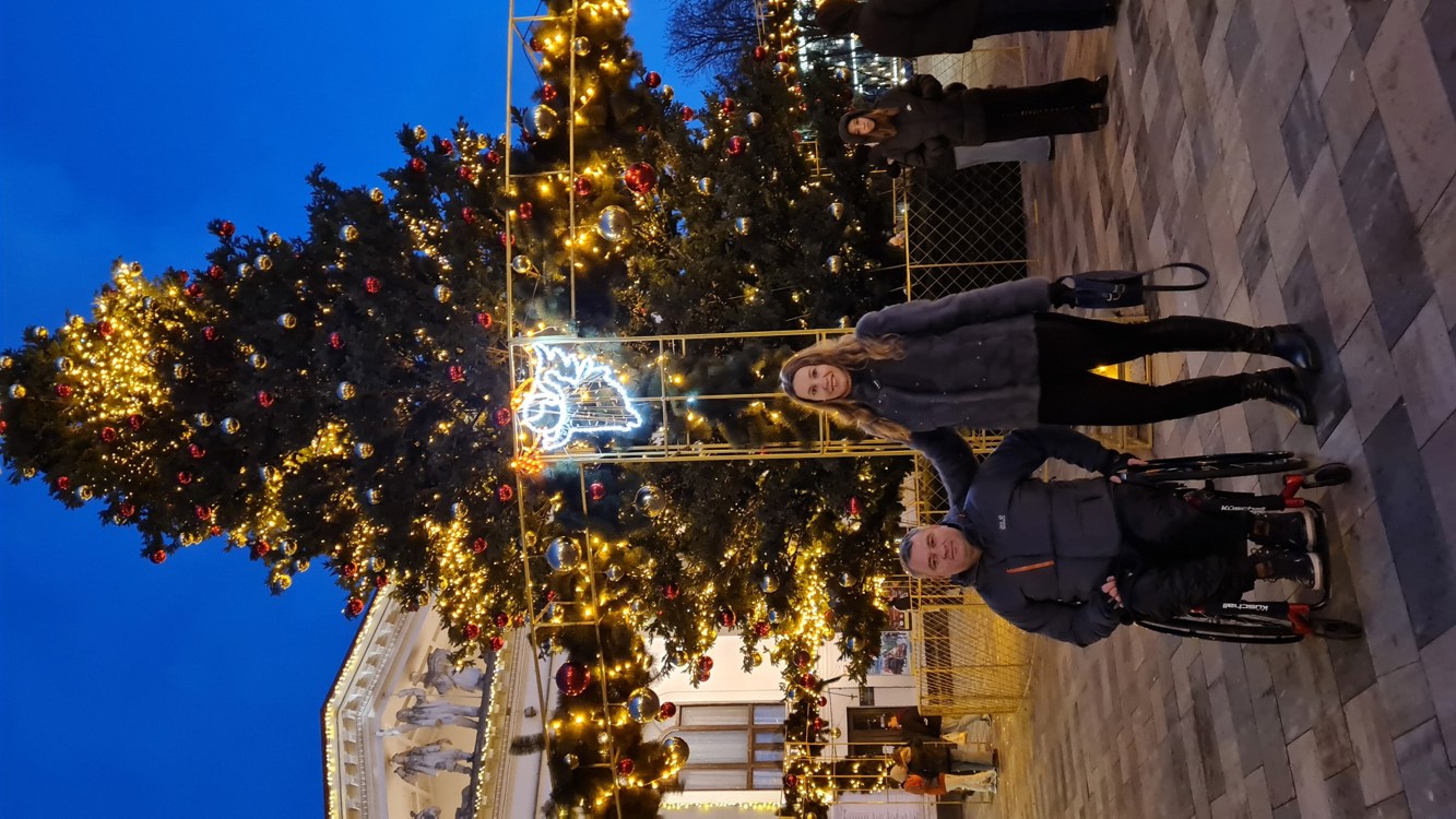 En mann i rullestol og en kvinne er foran et juletre og et teater i Ukraina. 