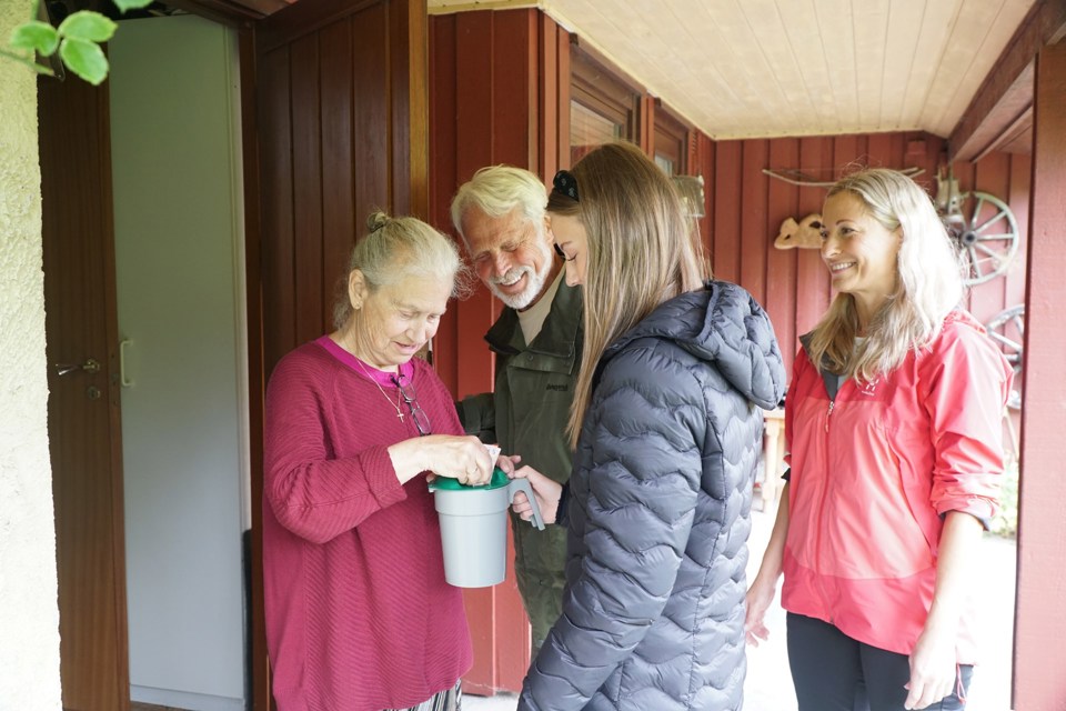 En morfar, mor og datter går med bøsse på dør. Her har en kvinne åpnet døren, og putter kontanter på bøssa.
