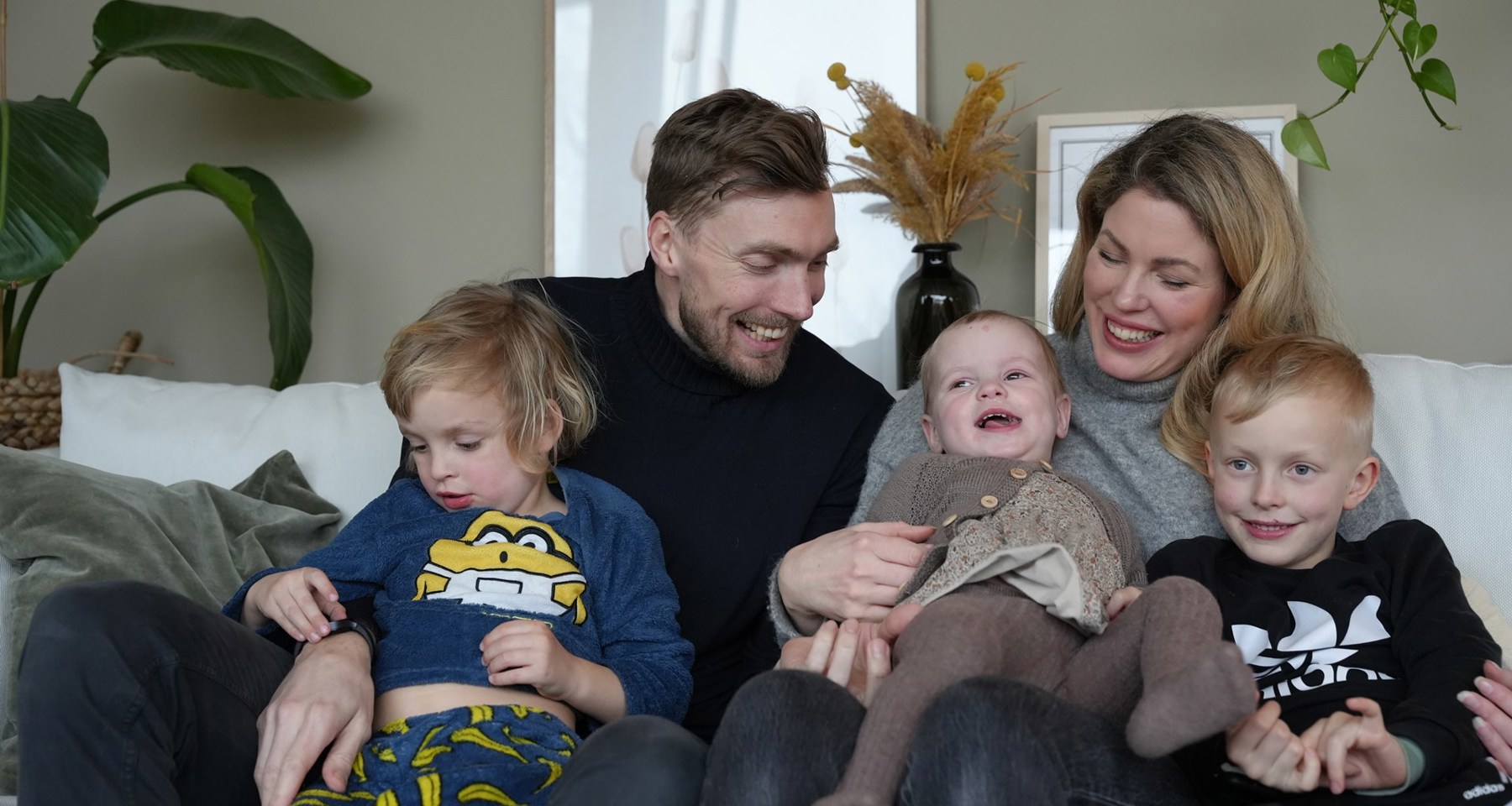En familie med to voksne og tre barn smiler og sitter i en sofa.